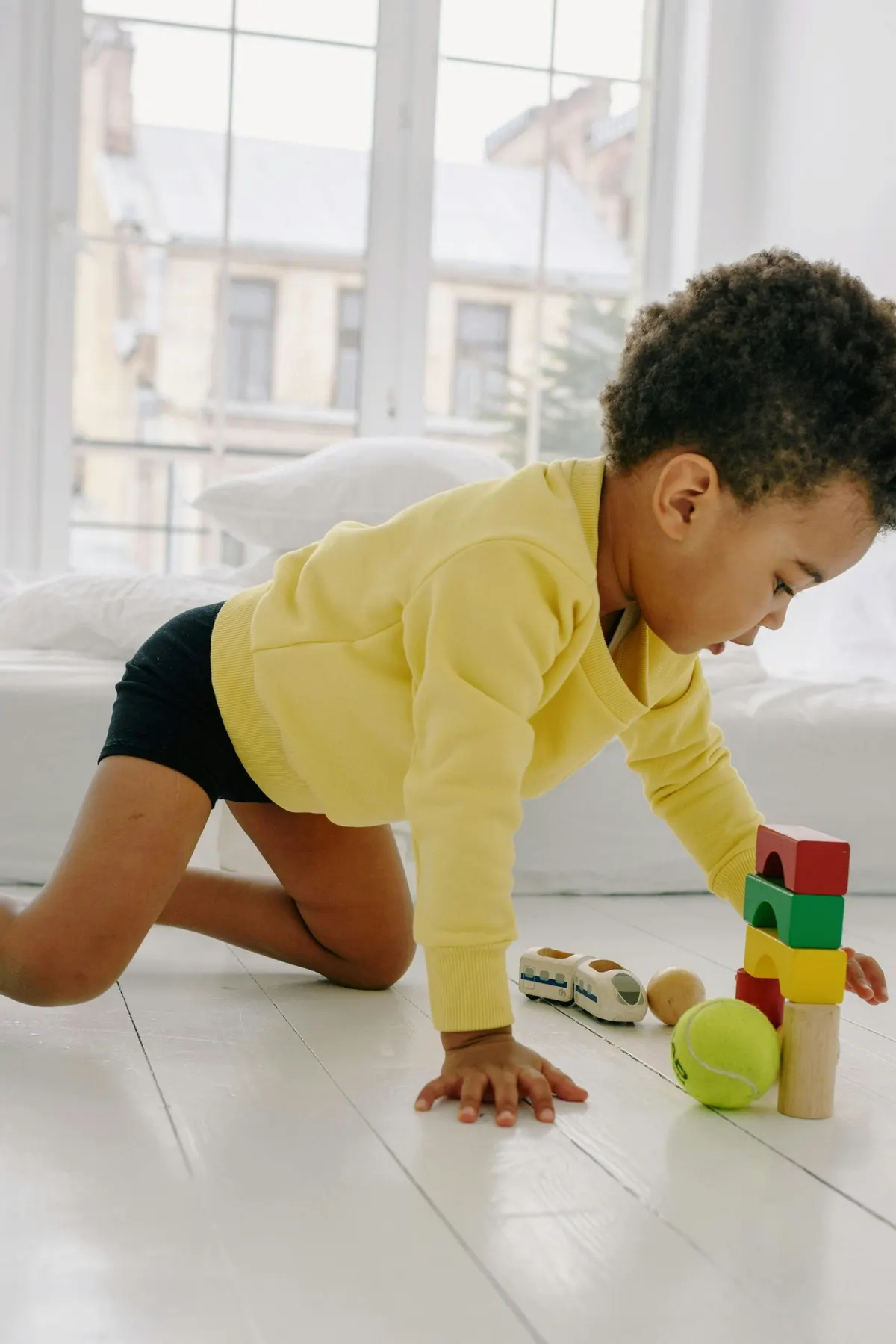A young child in a bright yellow sweatshirt playing with stacking blocks in a sunlit room
