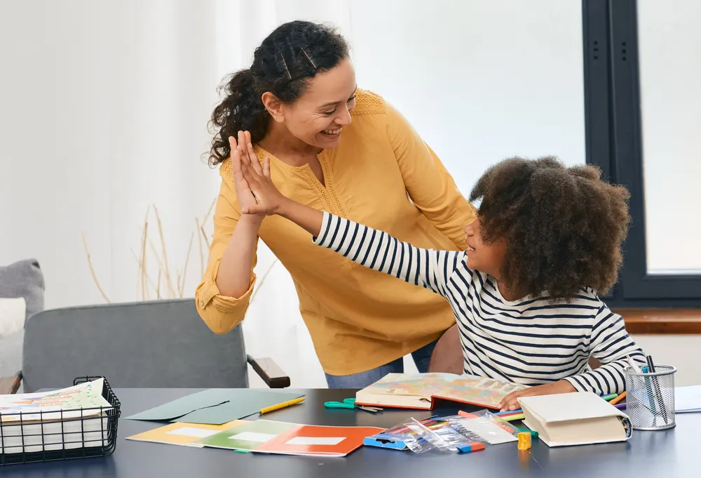 A smiling mother and her young daughter sharing a joyful high-five at a desk
